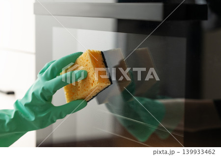 Cleaning the oven door with a sponge and a rubber glove, removing grease in a modern kitchen. Cleaning the oven door with a sponge and a rubber glove, removing grease in a modern kitchen. 139933462