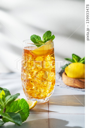 Iced tea with lemon and mint in a glass on a light tile background with shadows Iced tea with lemon and mint in a glass on a light tile background with shadows 139933478