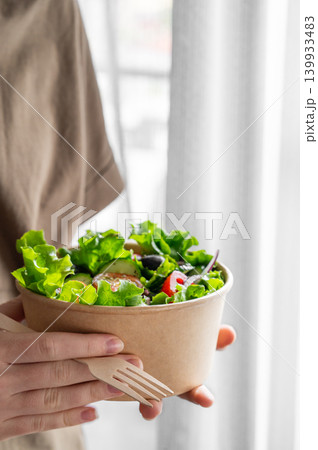 A woman holds a healthy vegetable salad in an eco-friendly takeaway bowl. A woman holds a healthy vegetable salad in an eco-friendly takeaway bowl. 139933483