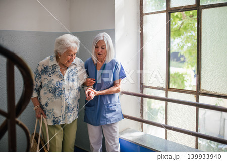 Female healthcare worker helping senior patient walking down the stairs. 139933940