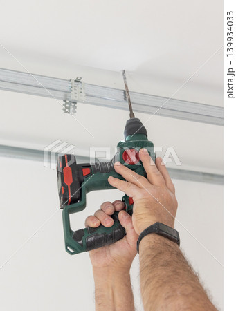Construction worker using drill on metal frame for drywall suspended ceiling in apartment renovation 139934033