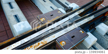 Rails fork junction with metal components and concrete supports, showcasing the connection between two railway tracks on a paved surface Rails fork junction with metal components and concrete supports, showcasing the connection between two railway tracks on a paved surface 139934061