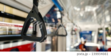 Black handle for holding passengers inside a public bus, with blurred interior elements and seating visible in the background, showcasing urban transportation features 139934081