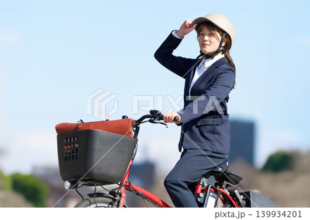 ヘルメットを着用して電動自転車で移動する女性会社員 139934201