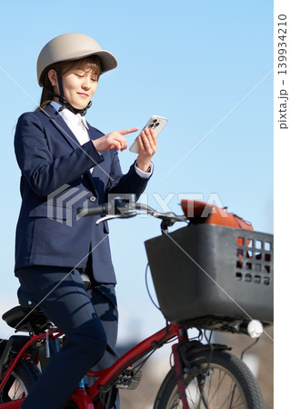自転車で移動中にスマートフォンを利用する女性会社員 自転車で移動中にスマートフォンを利用する女性会社員 139934210