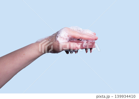 Hair pink scalp massager in woman hand with shampoo foam on blue background isolated. Image with copy space. Mock up for design and banner Hair pink scalp massager in woman hand with shampoo foam on blue background isolated. Image with copy space. Mock up for design and banner 139934410