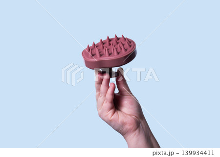 Pink scalp massager brush for hair treatment and care in human hand on blue background Pink scalp massager brush for hair treatment and care in human hand on blue background 139934411