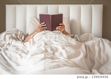 Young man reading book in bed at home. Relaxing in bed, reading a book Young man reading book in bed at home. Relaxing in bed, reading a book 139934456