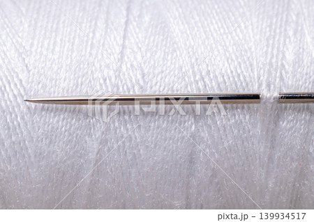 Sharp sewing needle on white thread spool background macro 139934517