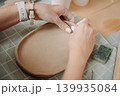 close-up female hands make a clay plate, align the shape with special tools in the workshop 139935084
