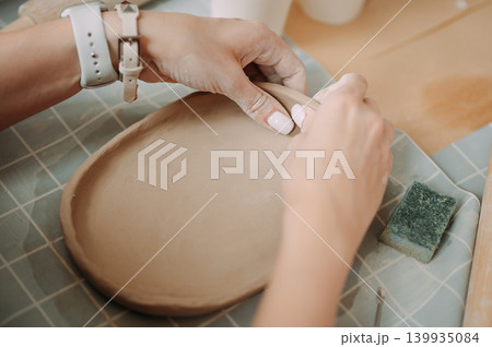 close-up female hands make a clay plate, align the shape with special tools in the workshop 139935084