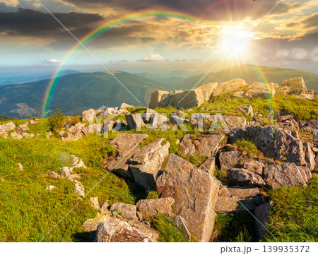 sunset over mountain landscape with stones and grass. view of carpthian mountains in summer. white sharp stones on the rolling hills on top of mountain range under blue sky. weather with rainbow 139935372