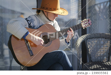 A woman in a cowboy hat is playing guitar on the porch of her ranch. She is sitting on a chair and enjoying what is happening. A student is learning to play the guitar. The musician gives a concert A woman in a cowboy hat is playing guitar on the porch of her ranch. She is sitting on a chair and enjoying what is happening. A student is learning to play the guitar. The musician gives a concert 139935561