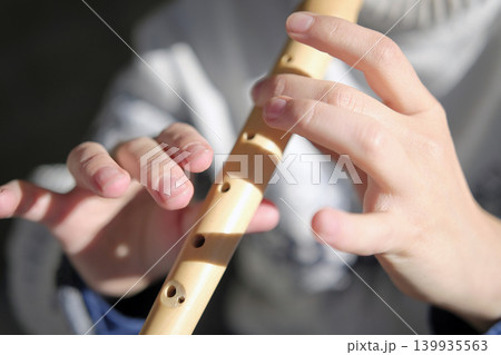 Close-up of a flutist's hand on a wooden flute. The piper holds a flute in his hands and plays it. The concept of relaxation and enjoyment is when the musician is focused on the instrument 139935563
