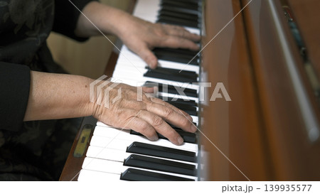 Close-up of the hands of an elderly pianist. An old woman plays the piano, the focus is on the hand and the keys. The concept of nostalgia and the beauty of music. Piano lessons. Music school Close-up of the hands of an elderly pianist. An old woman plays the piano, the focus is on the hand and the keys. The concept of nostalgia and the beauty of music. Piano lessons. Music school 139935577