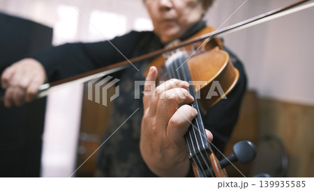 A woman plays the violin, close-up, focus on the hand and strings. An elderly violinist gives violin lessons. The musician is in a rush of inspiration A woman plays the violin, close-up, focus on the hand and strings. An elderly violinist gives violin lessons. The musician is in a rush of inspiration 139935585