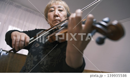 An elderly Asian woman is intently playing the violin, bottom view, focus on the face. An old violinist is learning a new tune. The musician is in a rush of inspiration An elderly Asian woman is intently playing the violin, bottom view, focus on the face. An old violinist is learning a new tune. The musician is in a rush of inspiration 139935586