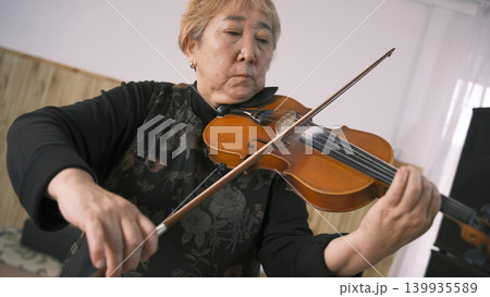 Portrait of a focused elderly Asian lady playing the violin. An old violinist gives violin lessons. The musician is playing his favorite tune. A teacher at a music school Portrait of a focused elderly Asian lady playing the violin. An old violinist gives violin lessons. The musician is playing his favorite tune. A teacher at a music school 139935589