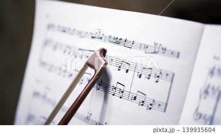 The bow from the violin points to the notes, close-up. A sheet of music with a beautiful melody. Music school. The composer is at work. The concept of music The bow from the violin points to the notes, close-up. A sheet of music with a beautiful melody. Music school. The composer is at work. The concept of music 139935604