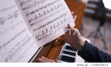 The musician is flipping through a music book, sitting at the piano, close-up. These are the notes of a piano piece, and this person is most likely a pianist or a music student 139935631