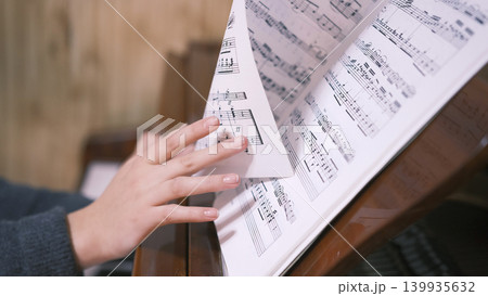 Music book, close-up. The musician turns the page with the notes of a piece of music. A pianist looks at the sheet music while playing the piano. A young female student 139935632