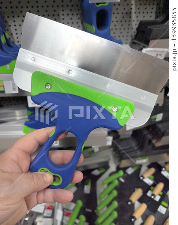Colorful scraper held in hand at hardware store for DIY projects Colorful scraper held in hand at hardware store for DIY projects 139935855