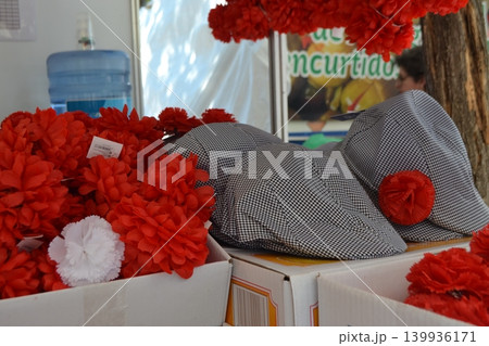 Checkered flat caps with red floral accessories on boxes for feria san isidro madrid market stall display and costume accessory background Checkered flat caps with red floral accessories on boxes for feria san isidro madrid market stall display and costume accessory background 139936171