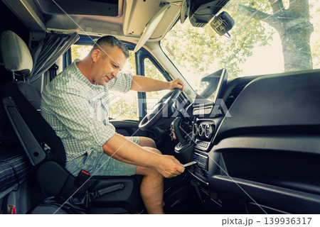 Side view of a middle-aged male professional driver sitting in a truck cabin workspace Side view of a middle-aged male professional driver sitting in a truck cabin workspace 139936317