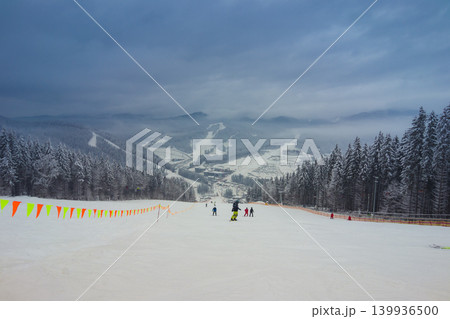 Cloudy day in the mountains and on the ski slope with a cable car and wooden houses. Wooden houses and Christmas trees in the snow. Carpathians. Ukraine Cloudy day in the mountains and on the ski slope with a cable car and wooden houses. Wooden houses and Christmas trees in the snow. Carpathians. Ukraine 139936500