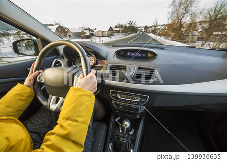 Modern car interior with driver female hands on steering wheel, winter snowy landscape outside. Safe driving concept. Modern car interior with driver female hands on steering wheel, winter snowy landscape outside. Safe driving concept. 139936635