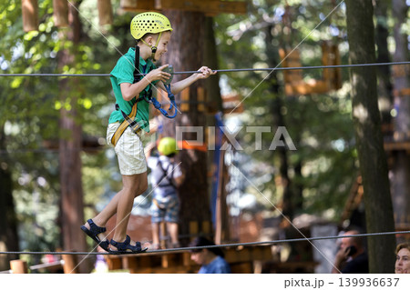 Young child boy in safety harness and helmet attached with carbine to cable on rope way in park. 139936637