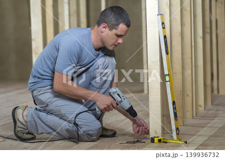 Young professional worker uses level and screwdriver installing wooden frame for future walls. Interior of attic room with oak floor under reconstruction. Renovation and improvement concept. Young professional worker uses level and screwdriver installing wooden frame for future walls. Interior of attic room with oak floor under reconstruction. Renovation and improvement concept. 139936732