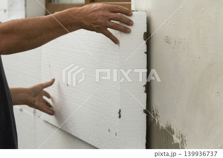 Worker hands installing white rigid polyurethane foam sheet on plastered brick wall. Modern technology, renovation, insulation concept. Worker hands installing white rigid polyurethane foam sheet on plastered brick wall. Modern technology, renovation, insulation concept. 139936737