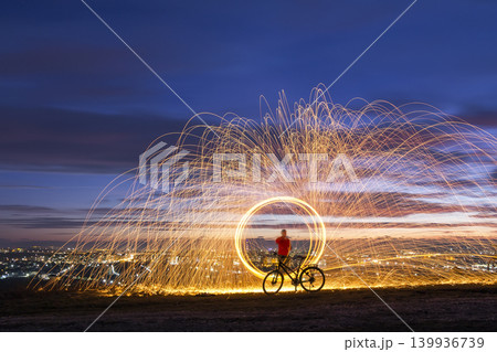Firework showers of hot glowing sparks from spinning steel wool in night city. Firework showers of hot glowing sparks from spinning steel wool in night city. 139936739