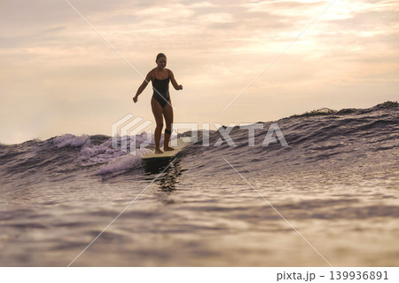 Woman Joyfully Dances Atop Surfboard During Sunset Amidst Gentle Waves Woman Joyfully Dances Atop Surfboard During Sunset Amidst Gentle Waves 139936891