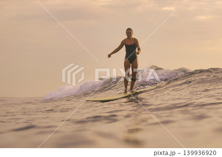 Confident Female Surfer Calmly Handles Gentle Coastal Surf At Dusk Confident Female Surfer Calmly Handles Gentle Coastal Surf At Dusk 139936920