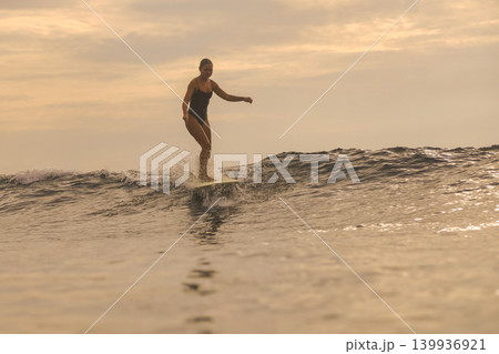 Calm Woman Balances On Surfboard As Bright Sunset Illuminates Ocean Calm Woman Balances On Surfboard As Bright Sunset Illuminates Ocean 139936921