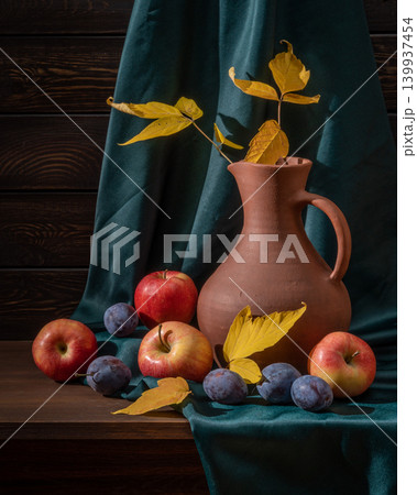 Autumn Still Life With Yellow Leaves in a Brown Jug Among Apples and Plums on Green Fabric Autumn Still Life With Yellow Leaves in a Brown Jug Among Apples and Plums on Green Fabric 139937454