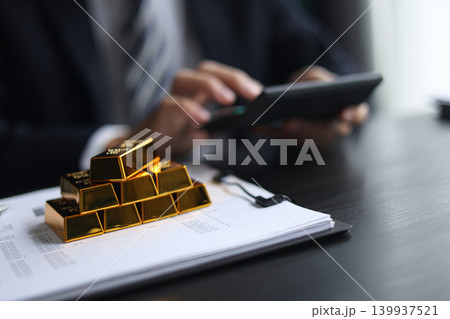 Gold volatility. Businessman calculating profit from fine gold bar investments. 139937521
