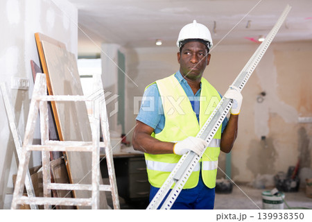African-american man builder carrying metallic profile while working in room African-american man builder carrying metallic profile while working in room 139938350