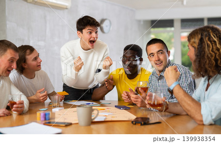 Cheerful guy playing board game with male friends Cheerful guy playing board game with male friends 139938354