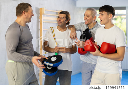 Four men of different ages in gym at group training session with sports equipment speaking 139941853