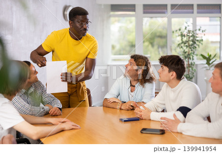 Middle-aged man instructor explaining the topic to group of guys around the table Middle-aged man instructor explaining the topic to group of guys around the table 139941954