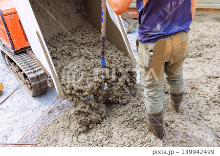 Workers are pouring concrete from tracked wheelbarrow onto ground for building purposes 139942499