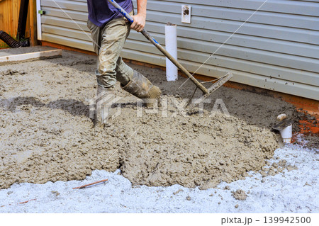 Worker uses level tool to smooth out wet concrete at home construction site 139942500