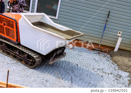 Concrete buggy is on construction site, moving wet cement across gravel while workers prepare for installation. Concrete buggy is on construction site, moving wet cement across gravel while workers prepare for installation. 139942501