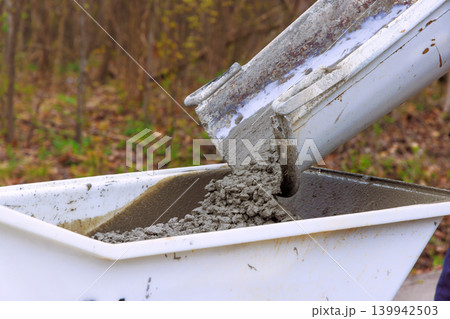 Workers use chute to pour fresh concrete into dumper wheelbarrow on an active construction site 139942503