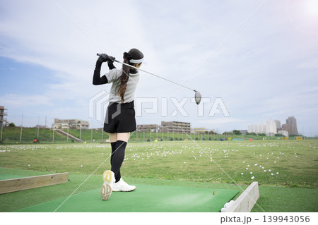 打ちっぱなしのゴルフ練習場でドライバーショットをスウィングする若い女性のゴルファーのスポーツイメージ 139943056