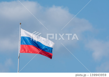 Russian tricolor flag waving in the wind against a blue sky. Fieldbird sits on a branch in spring with a blurred background. 139943959