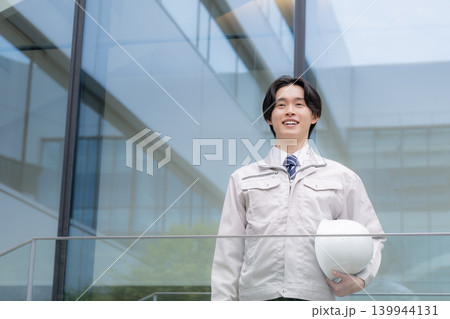 都会のビル背景で笑顔を見せる若手男性技術者と建設キャリアイメージ 就活やキャリアと成長、チャレンジ 都会のビル背景で笑顔を見せる若手男性技術者と建設キャリアイメージ 就活やキャリアと成長、チャレンジ 139944131